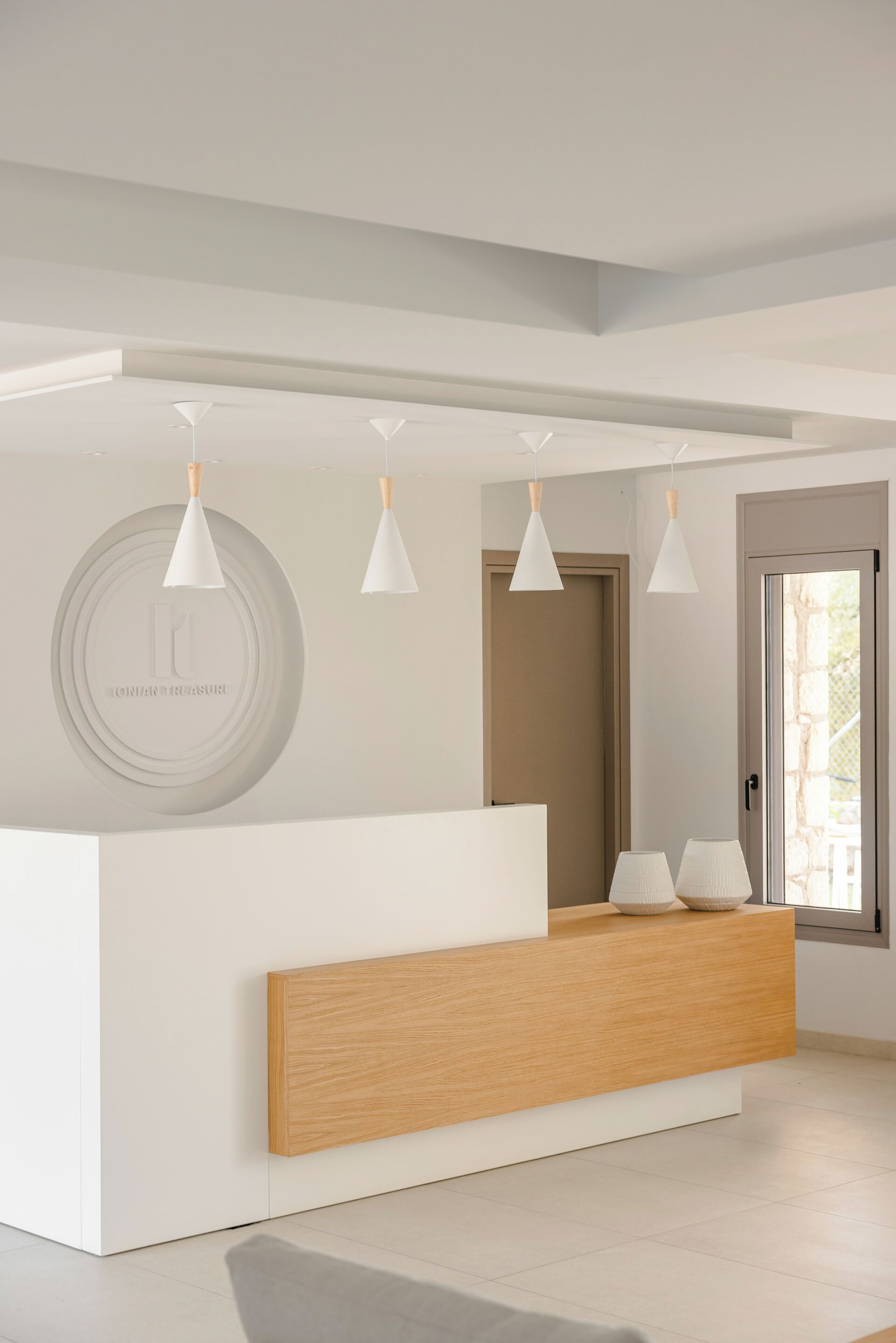 Un espace d’accueil doté d’un comptoir de réception en bois, de luminaires suspendus blancs et d’un logo circulaire sur le mur.
