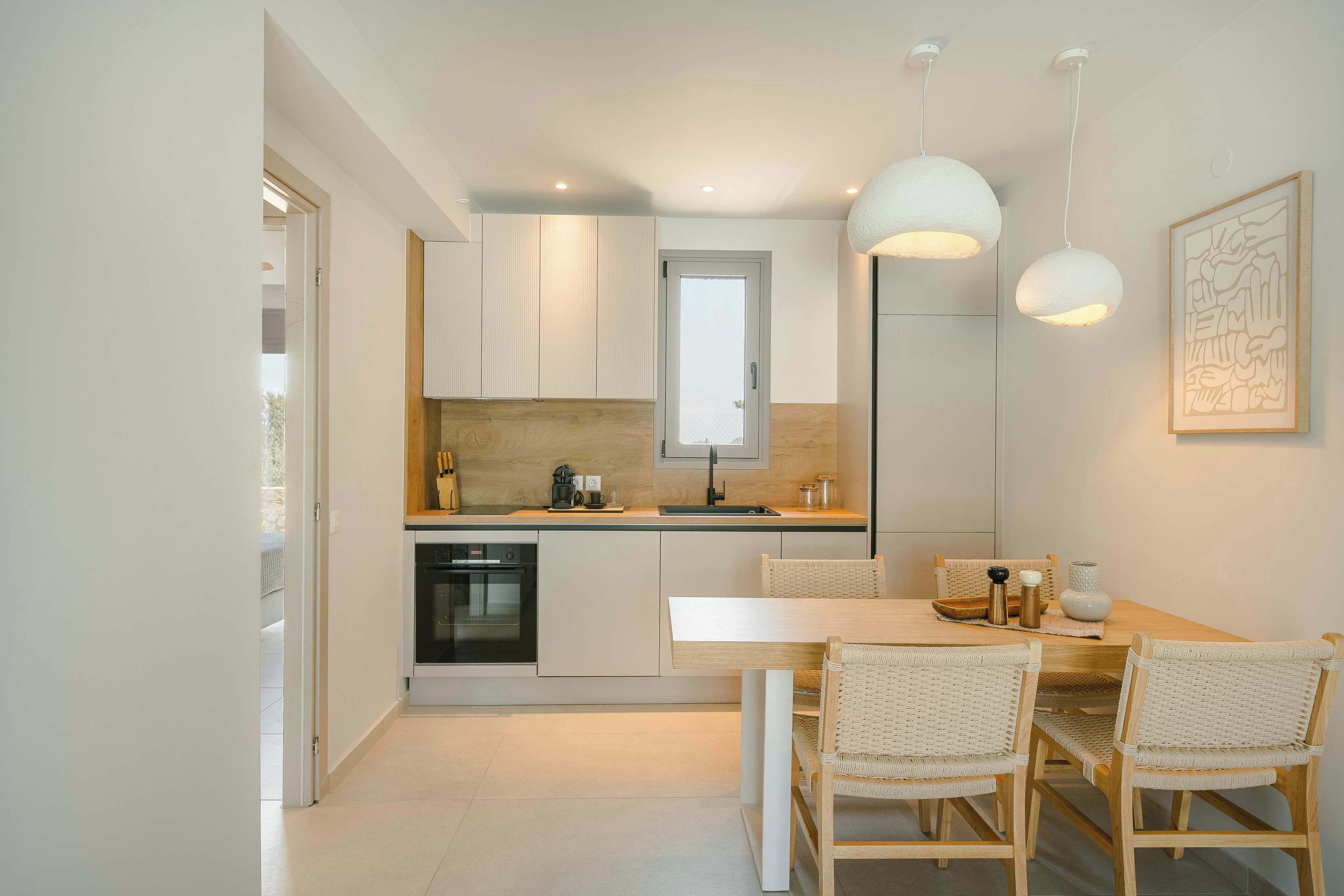 A modern kitchen with white cabinets, a built-in oven, and a dining area with a wooden table and wicker chairs.