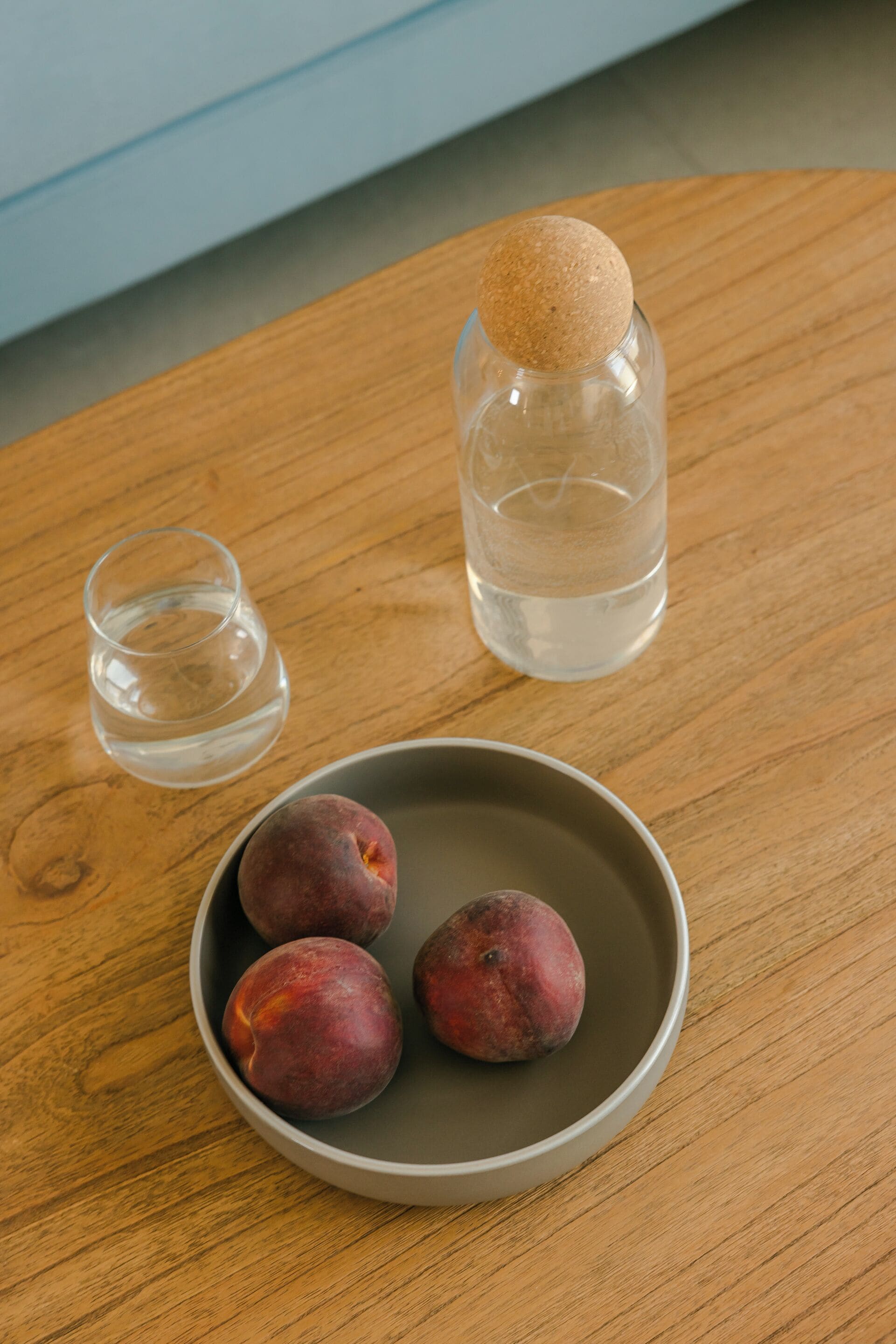 A wooden table with a bowl of fruit, a glass of water, and a bottle of water.
