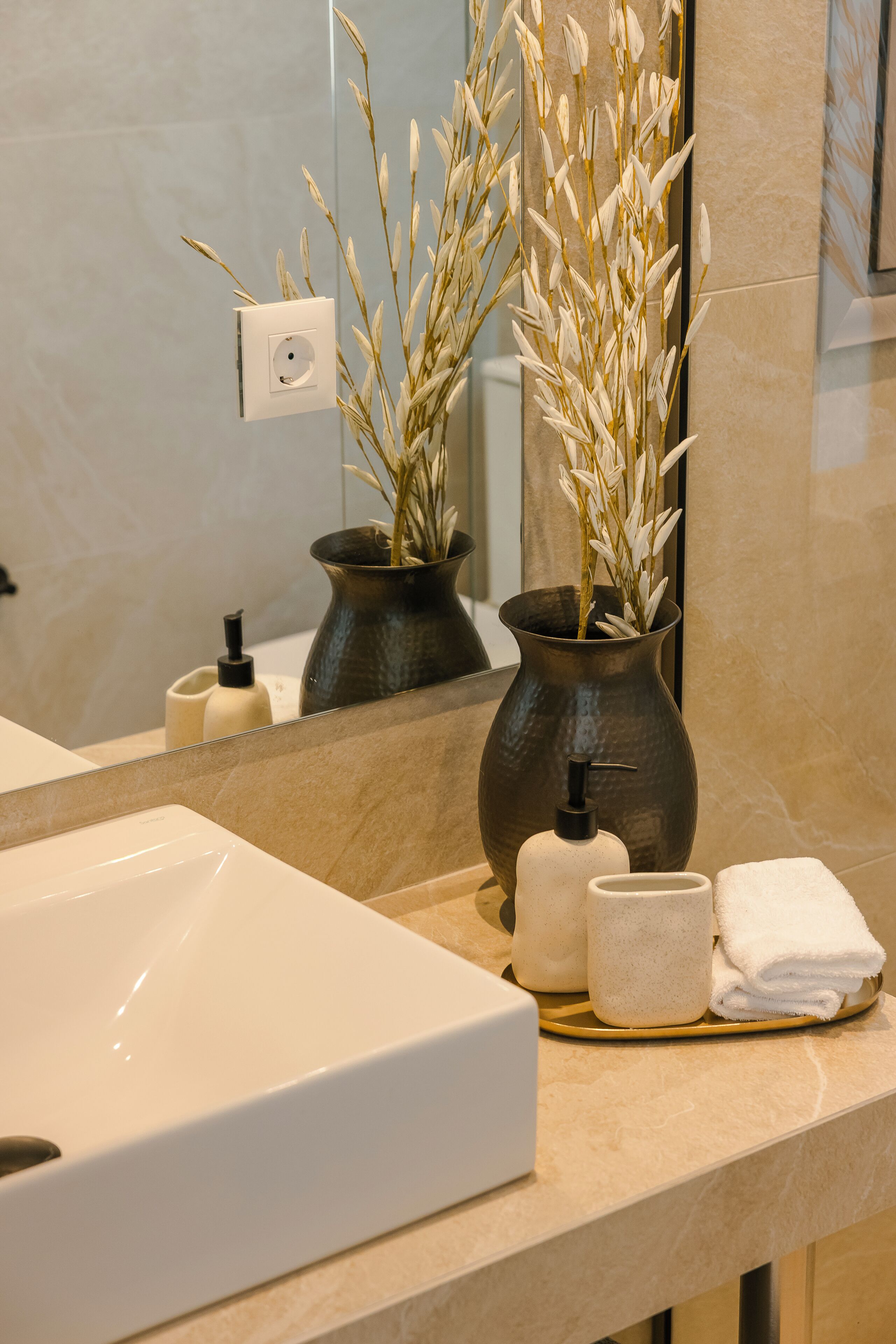 A bathroom with a white sink, two dark vases with dried plants, a soap dispenser, and a towel rack.