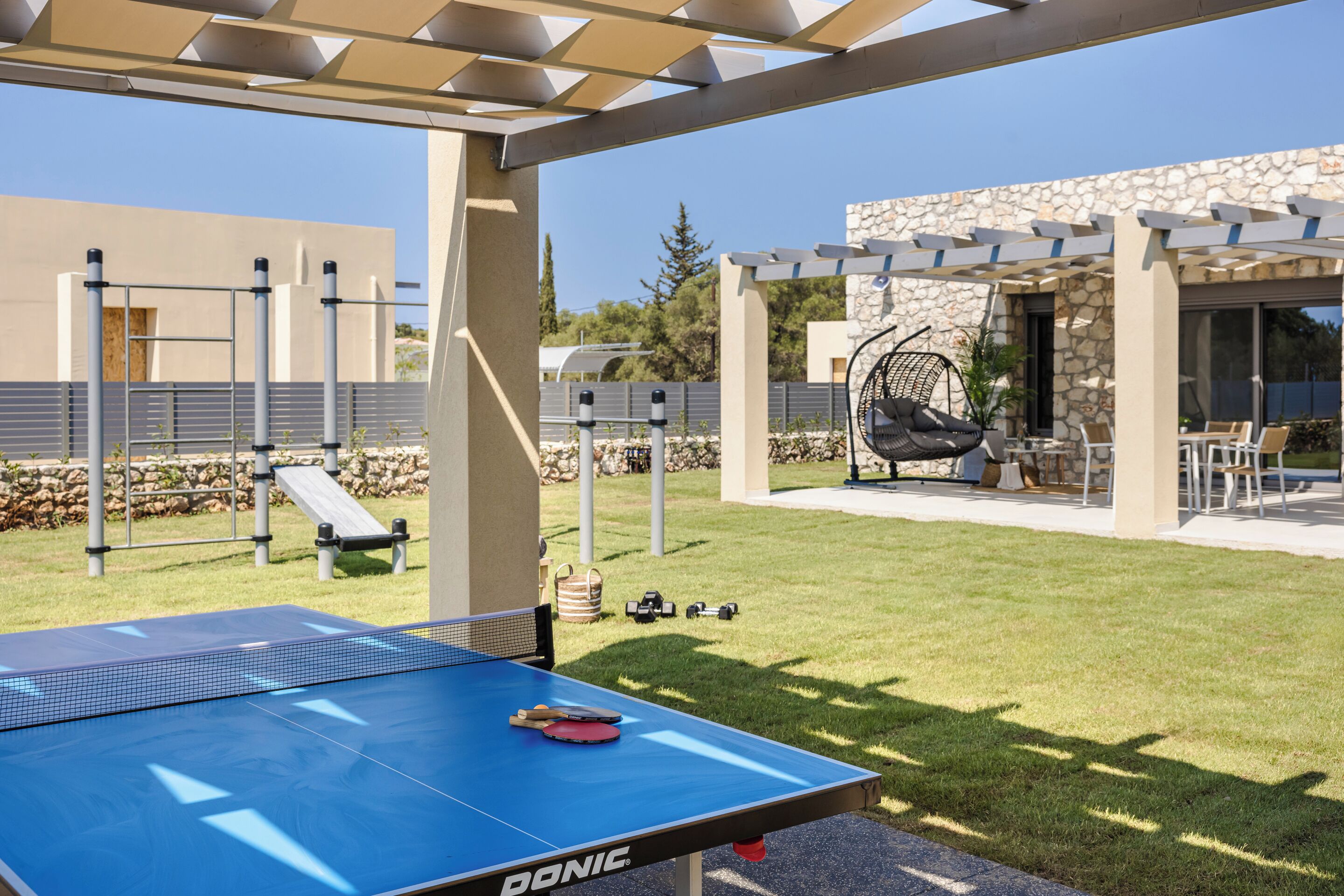 Una mesa de ping pong al aire libre con red, rodeada por una estructura de pérgola.
