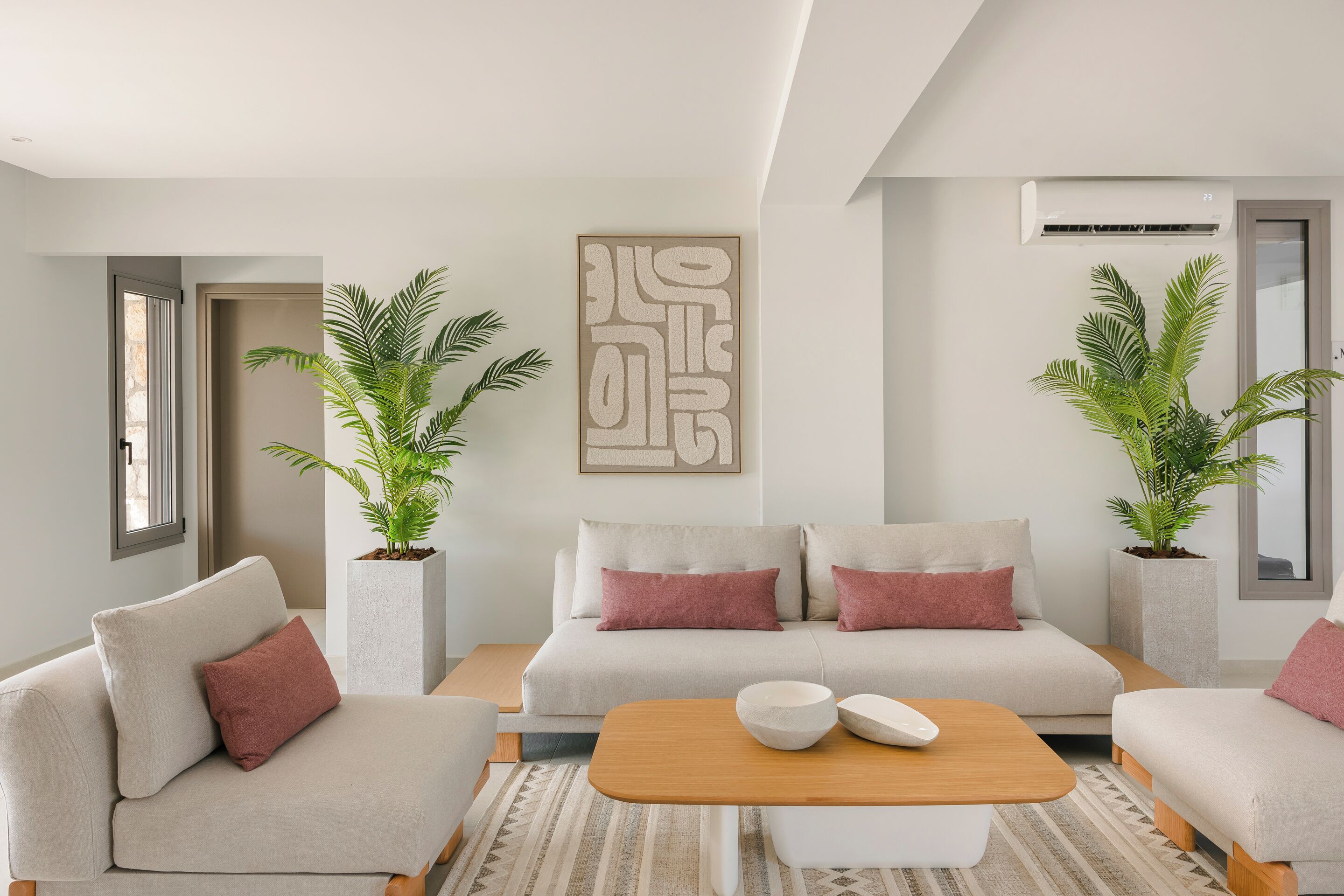 Una sala de estar moderna con un sofá beige, dos plantas en macetas, una mesa de centro de madera y una gran obra de arte abstracta en la pared.