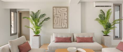 Een moderne woonkamer met een beige zithoek, twee potplanten, een houten salontafel en een groot abstract kunstwerk aan de muur.