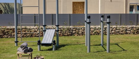 Un espacio exterior de gimnasio con equipo de ejercicio, un banco de madera y un perchero para toallas.