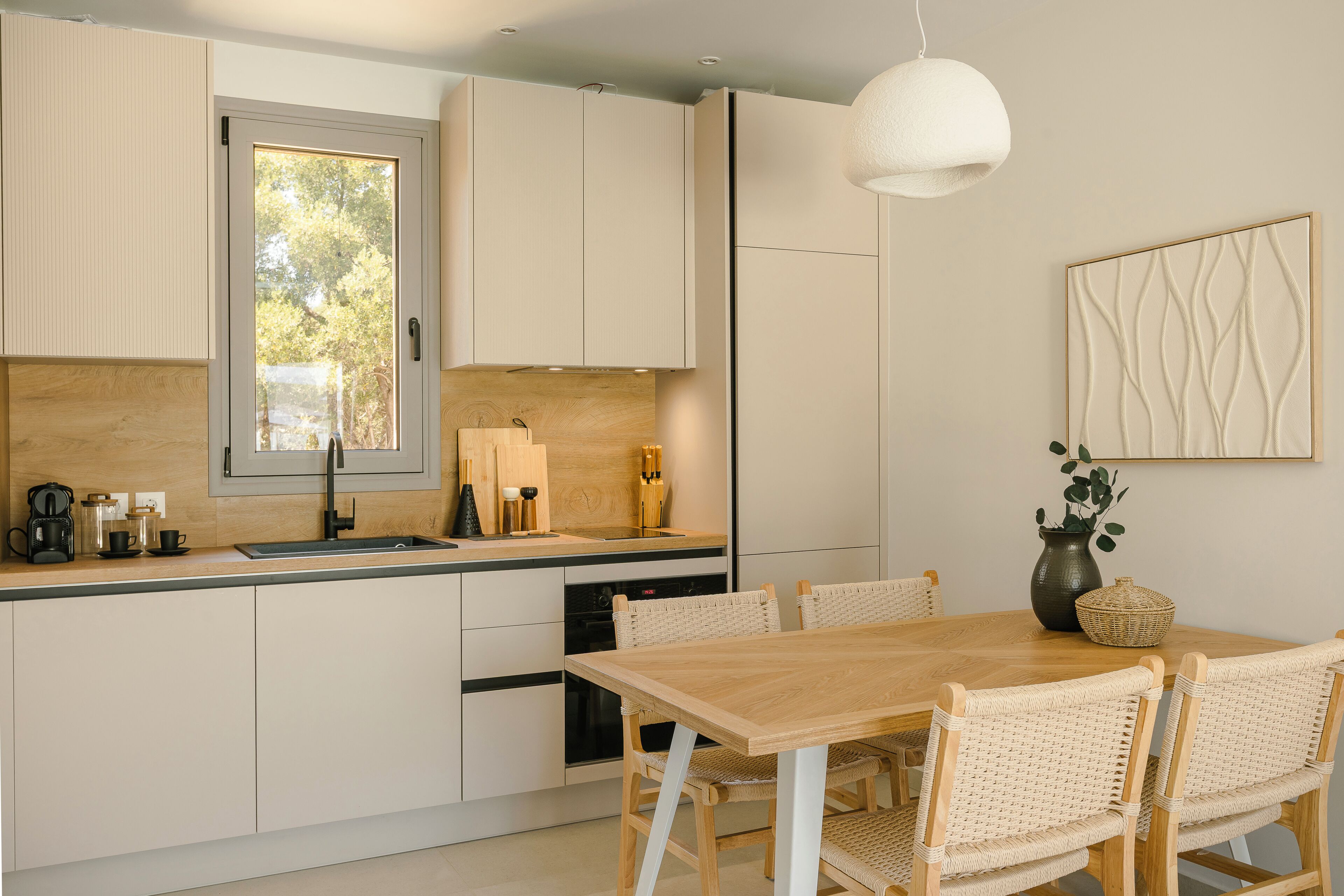 Une cuisine moderne avec une table et des chaises en bois, un four encastré et une grande fenêtre.