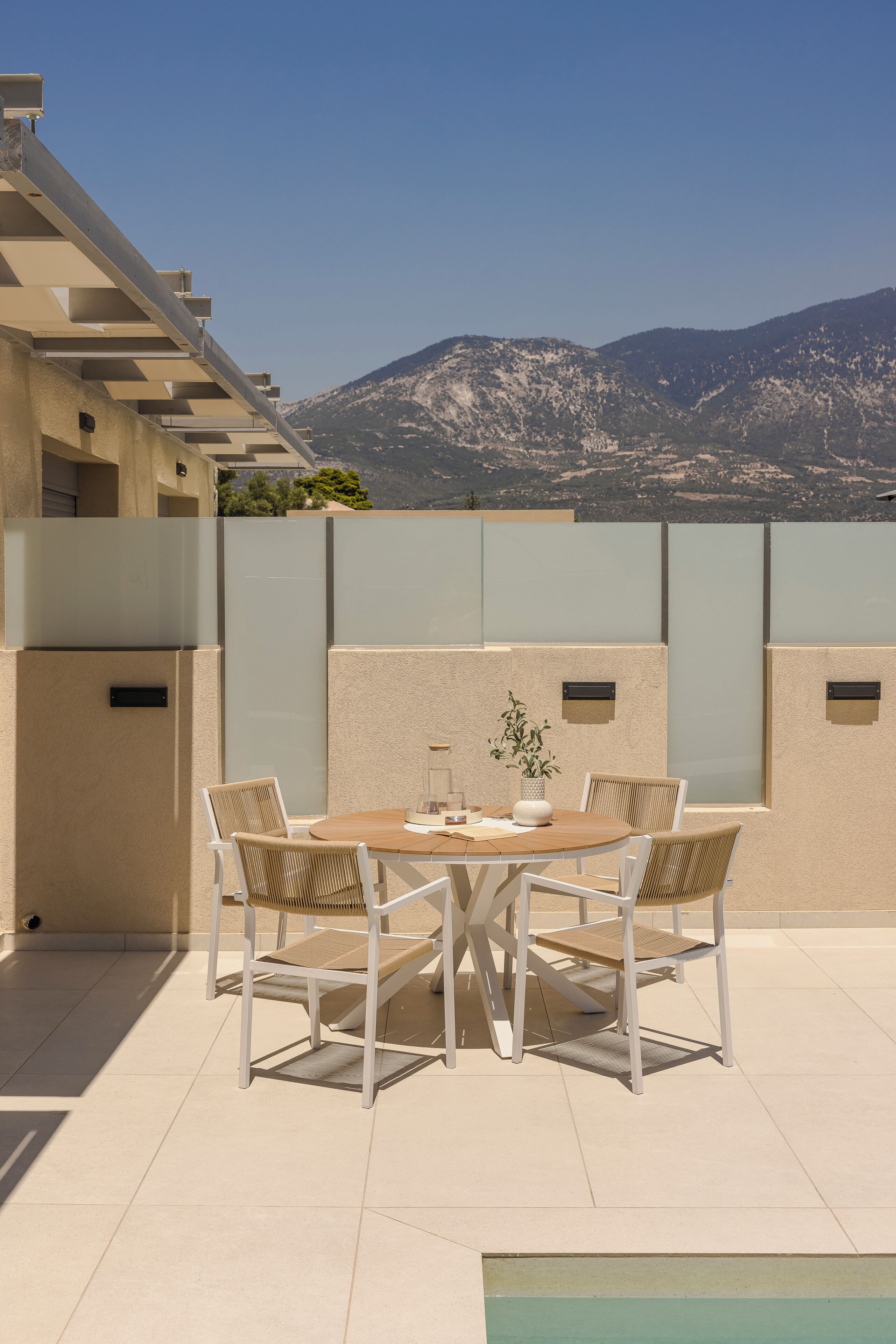 Eine Terrasse mit Tisch und Stühlen, einem Blumentopf und Blick auf Berge.