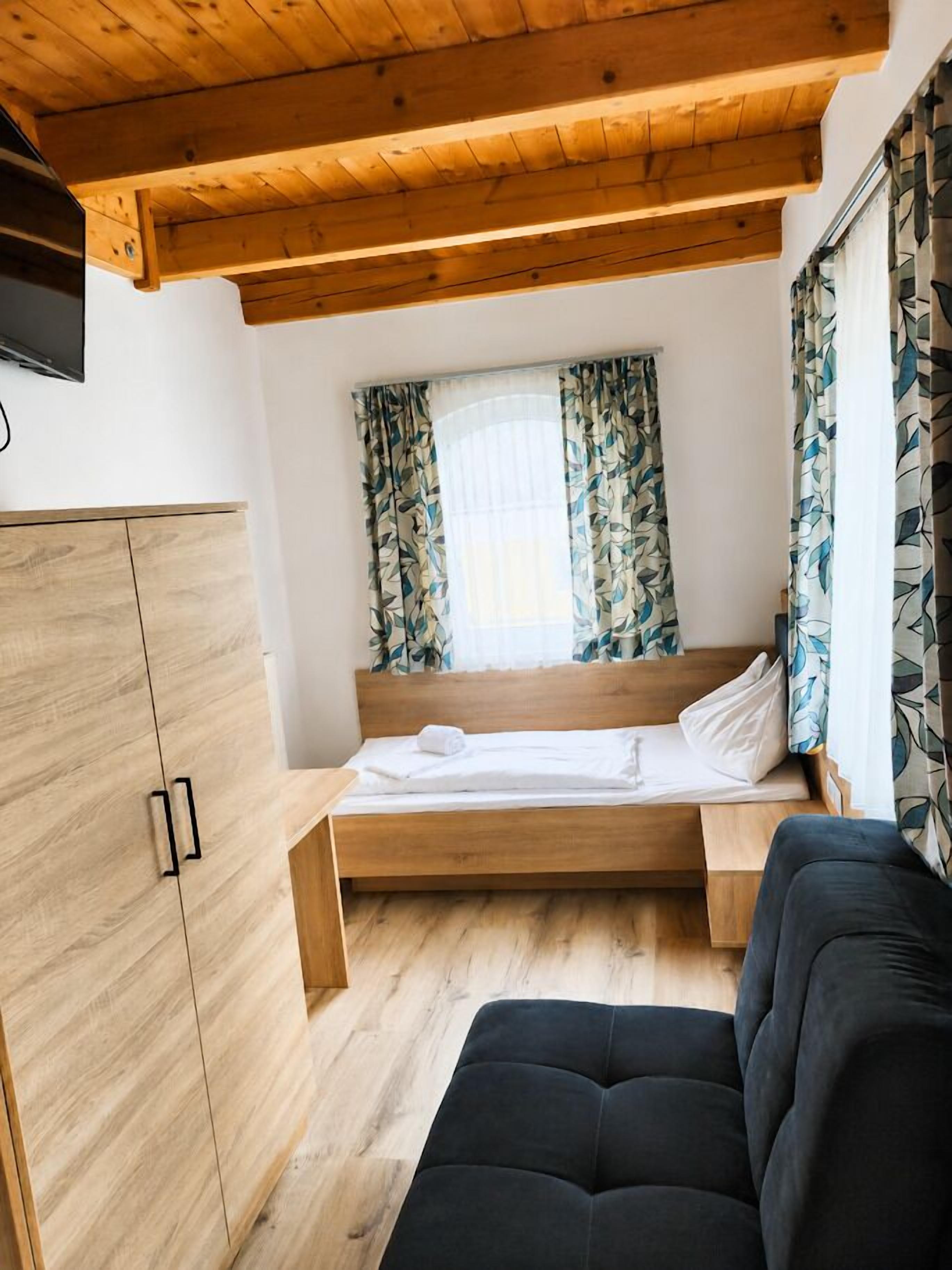 Un dormitorio con cama, armario, sofá y ventana con cortinas.