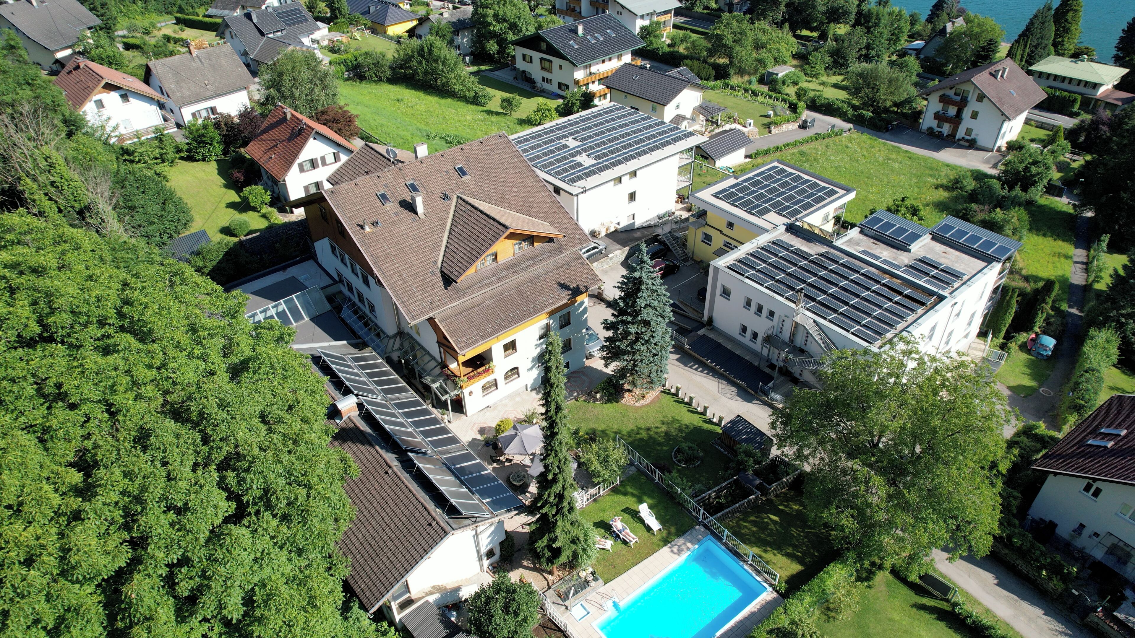 An aerial view of a residential area with multiple houses, some with solar panels, a swimming pool, and a well-maintained lawn.