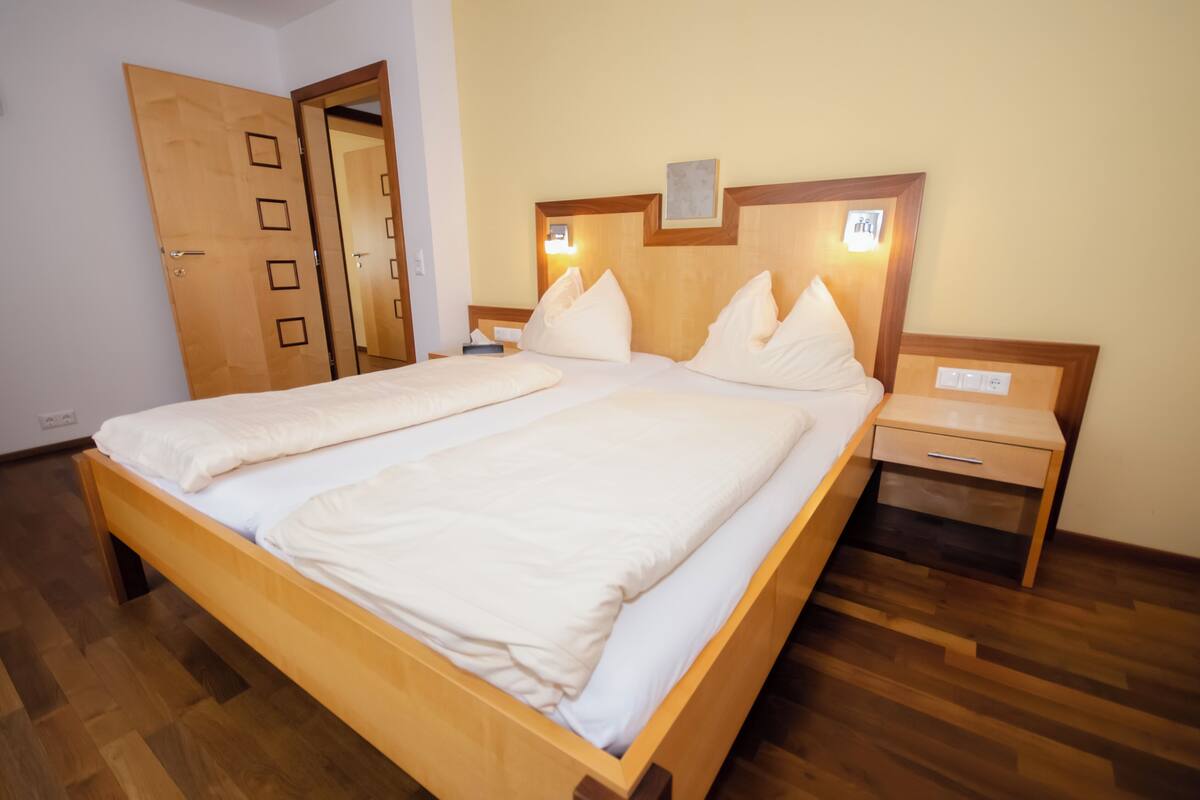 A double bed with a wooden frame, a nightstand with a drawer, and a door with a mirror.