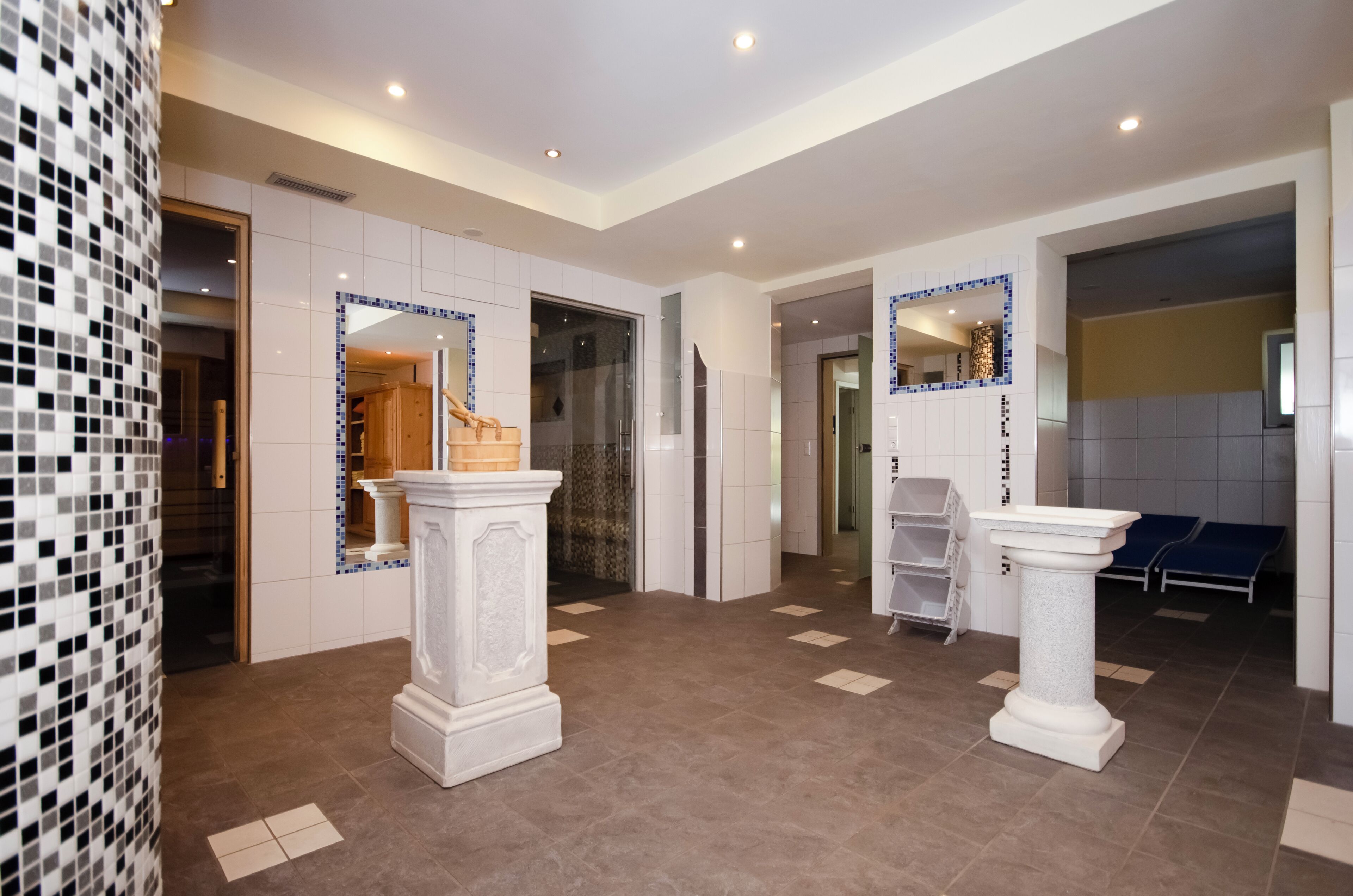 A spacious lobby with a tiled floor, white walls, and two columns. There is a reception desk and a seating area with blue chairs.