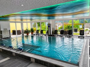 An indoor swimming pool with clear glass walls, lounge chairs, and a view of greenery outside. - Familienhotel Steindl (Millstatt)