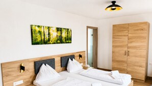 A double bed with white linens, a wooden headboard, a bedside table, a wardrobe, and a forest-themed wall art. - Familienhotel Steindl (Millstatt)