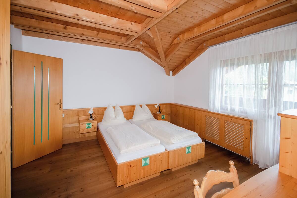 A wooden bedroom with a bed, bedside tables, and a window with curtains.