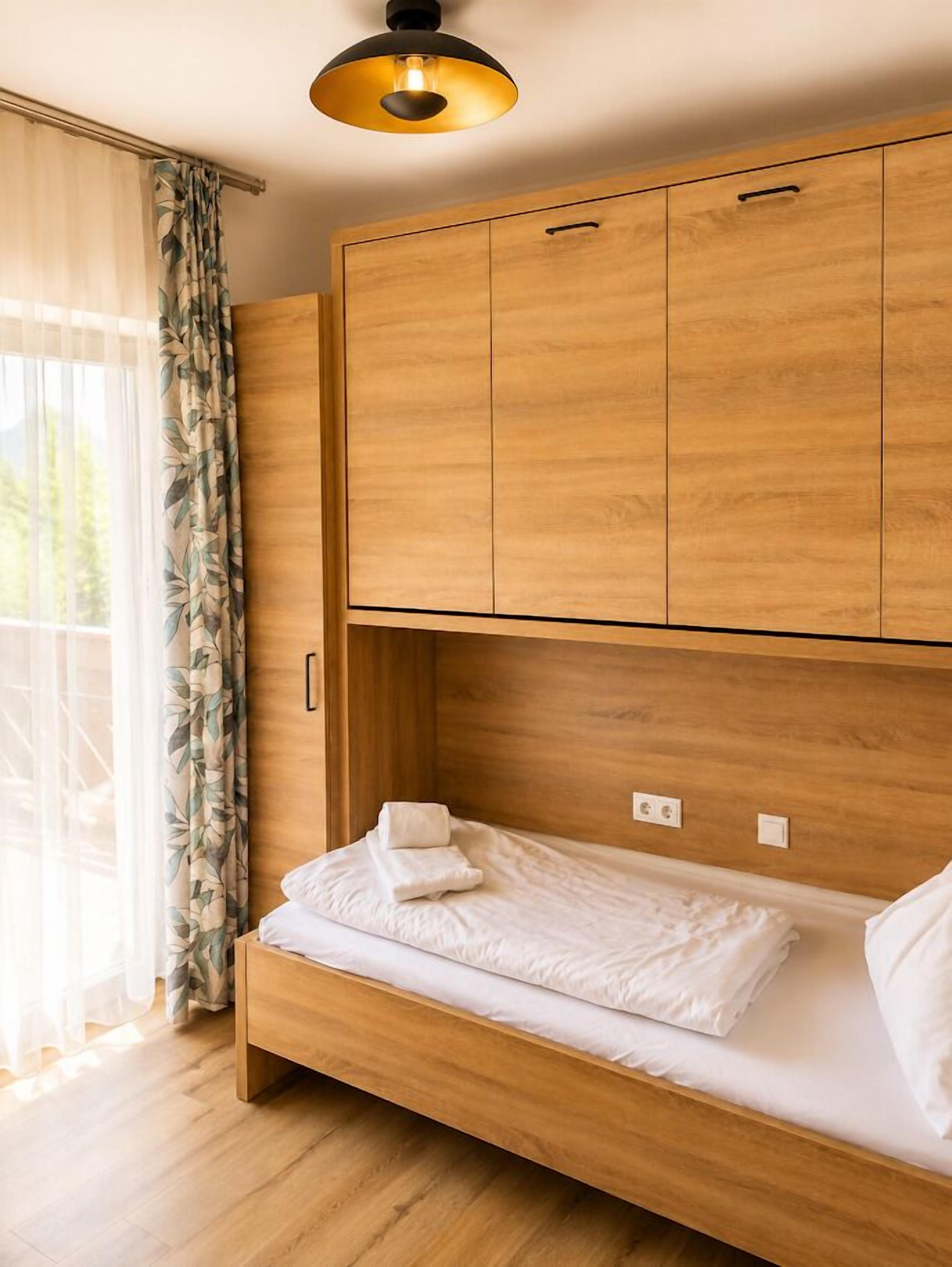 A room with a bed, wooden wardrobe, and a window with curtains.