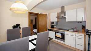 A compact kitchen with white cabinets, a microwave, a stove, and a sink. There is a dining area with a table and chairs. - Familienhotel Steindl (Millstatt)