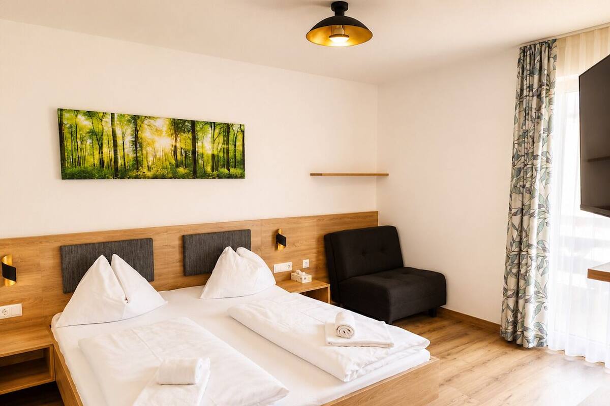 A hotel room with a bed, a chair, a painting, and a window with curtains.