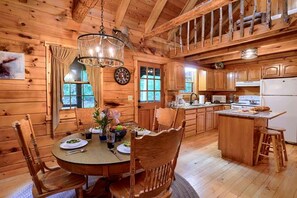 A wooden cabin interior with a dining area, kitchen, and a large window. - Cozy Log Cabin for an Ohio Outdoor Adventure near Hocking Hills State Park (New Plymouth)
