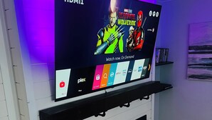 Ein Flachbildfernseher an einer weißen Wand befestigt, darunter ein Regal mit verschiedenen Mediensymbolen.
