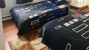 Ein Schlafzimmer mit zwei Betten, einem Deckenventilator, einem Fenster mit Vorhängen, einer Wandablage mit dekorativen Gegenständen und einem Nachttisch mit Lampe.