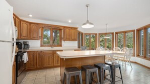 Eine moderne Küche mit Holzausstattung, einer großen Kochinsel mit Sitzgelegenheiten und großen Fenstern mit Blick auf Bäume.