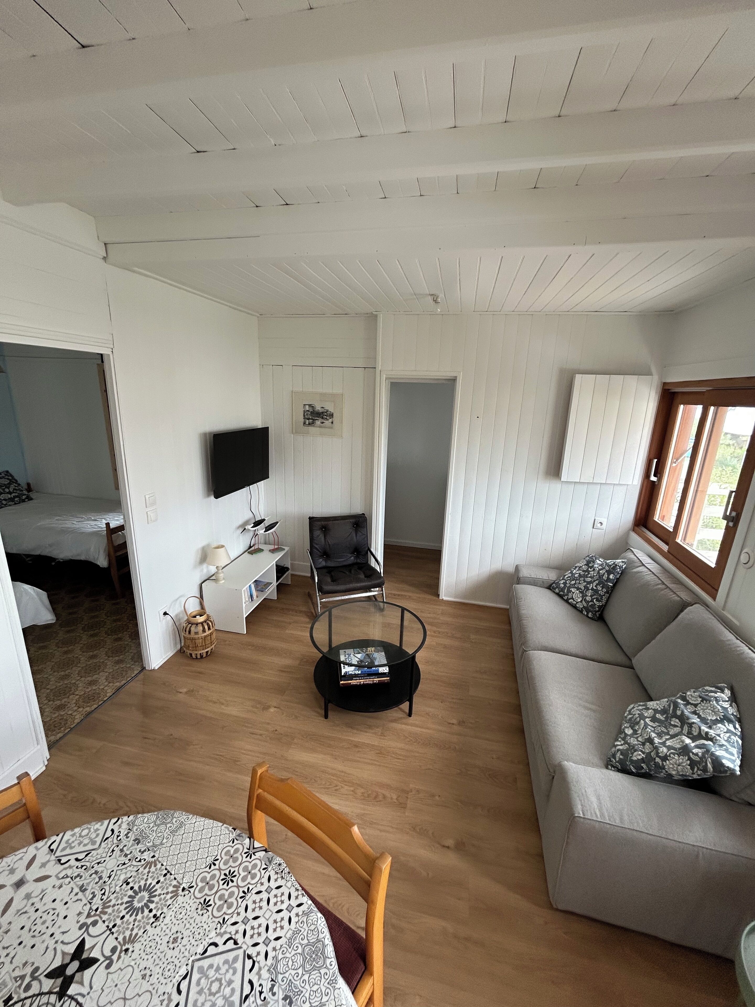 A spacious living area with a sofa, a round coffee table, a television, and a dining table with a patterned tablecloth.