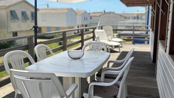 Un espace extérieur abrité, avec une table et des chaises blanches, des parasols et une vue sur des maisons en arrière-plan.