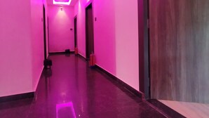 Um corredor com iluminação rosa, piso escuro e uma porta de madeira com o número 103.