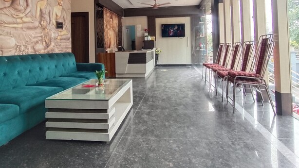 Um hall de hotel moderno com um sofá verde-água, uma mesa de centro de vidro, um balcão de recepção e uma fileira de cadeiras vermelhas.