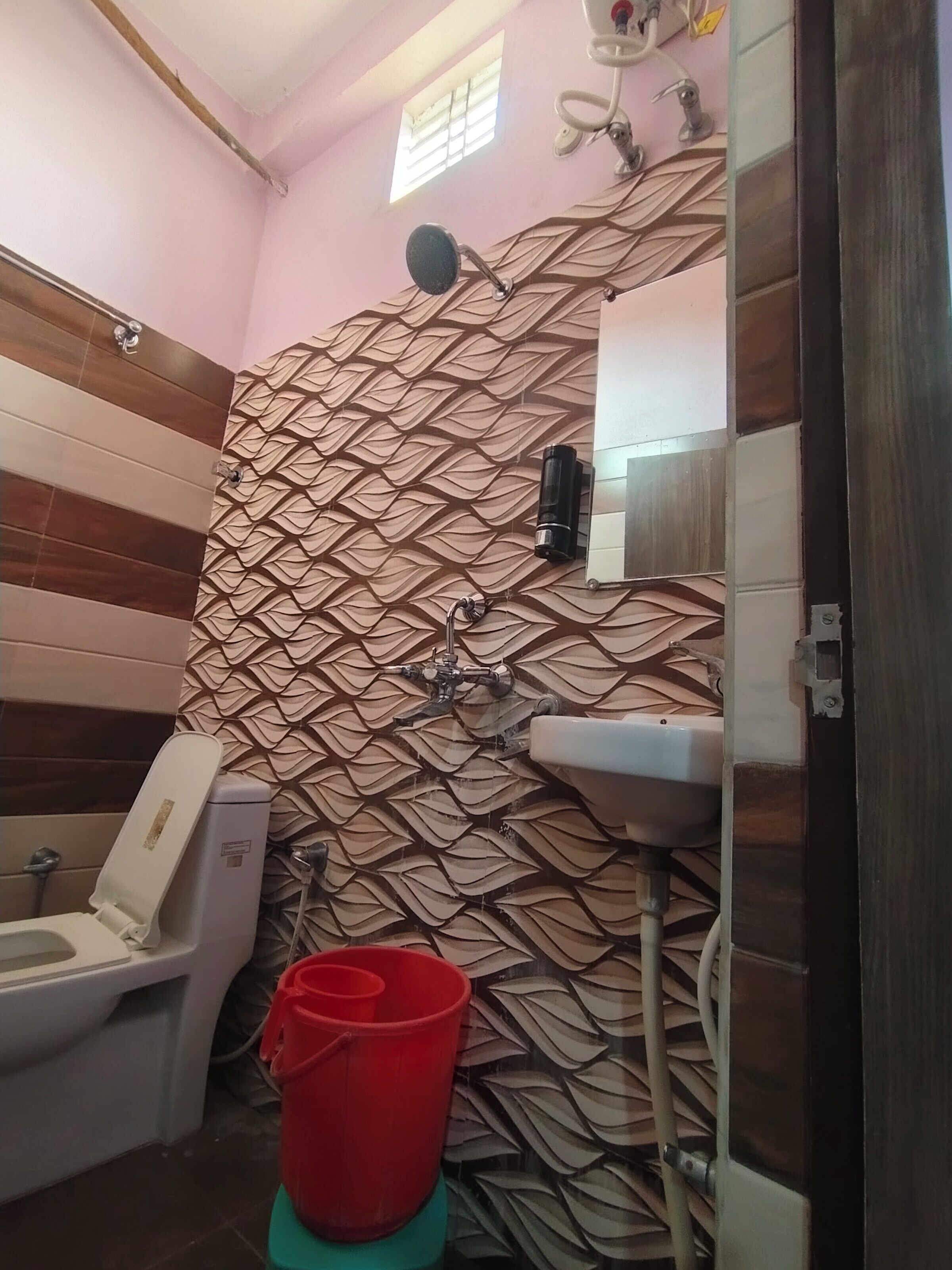 A bathroom with a patterned wall, a toilet, a sink, and a red bucket.