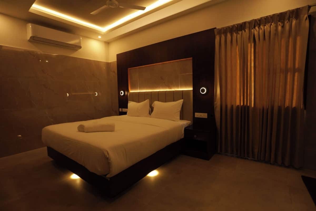 Een moderne hotelkamer met een groot bed, een hoofdbord met ingebouwde verlichting, een nachtkastje en een raam met gordijnen.