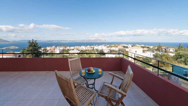 Un balcón con mesa y sillas, con vistas a un pueblo costero y al mar.