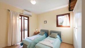 Un dormitorio con dos camas, una ventana, un equipo de aire acondicionado y una puerta.
