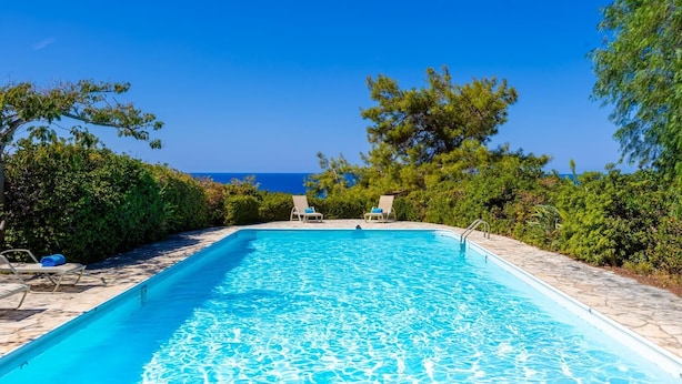 A rectangular swimming pool with clear blue water, surrounded by stone tiles and lush greenery. - Villa Sea Pines in Nea Dimmata (Nea Dimmata)