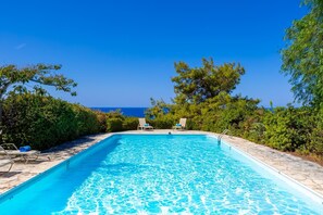 A rectangular swimming pool with clear blue water, surrounded by stone tiles and lush greenery. - Villa Sea Pines in Nea Dimmata (Nea Dimmata)