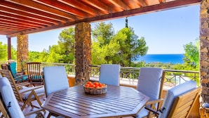 A covered outdoor seating area with a table and chairs, a stone pillar, and a view of the sea. - Villa Sea Pines in Nea Dimmata (Nea Dimmata)