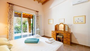 A bedroom with a bed, a wooden dresser, a mirror, and a window with curtains. - Villa Sea Pines in Nea Dimmata (Nea Dimmata)