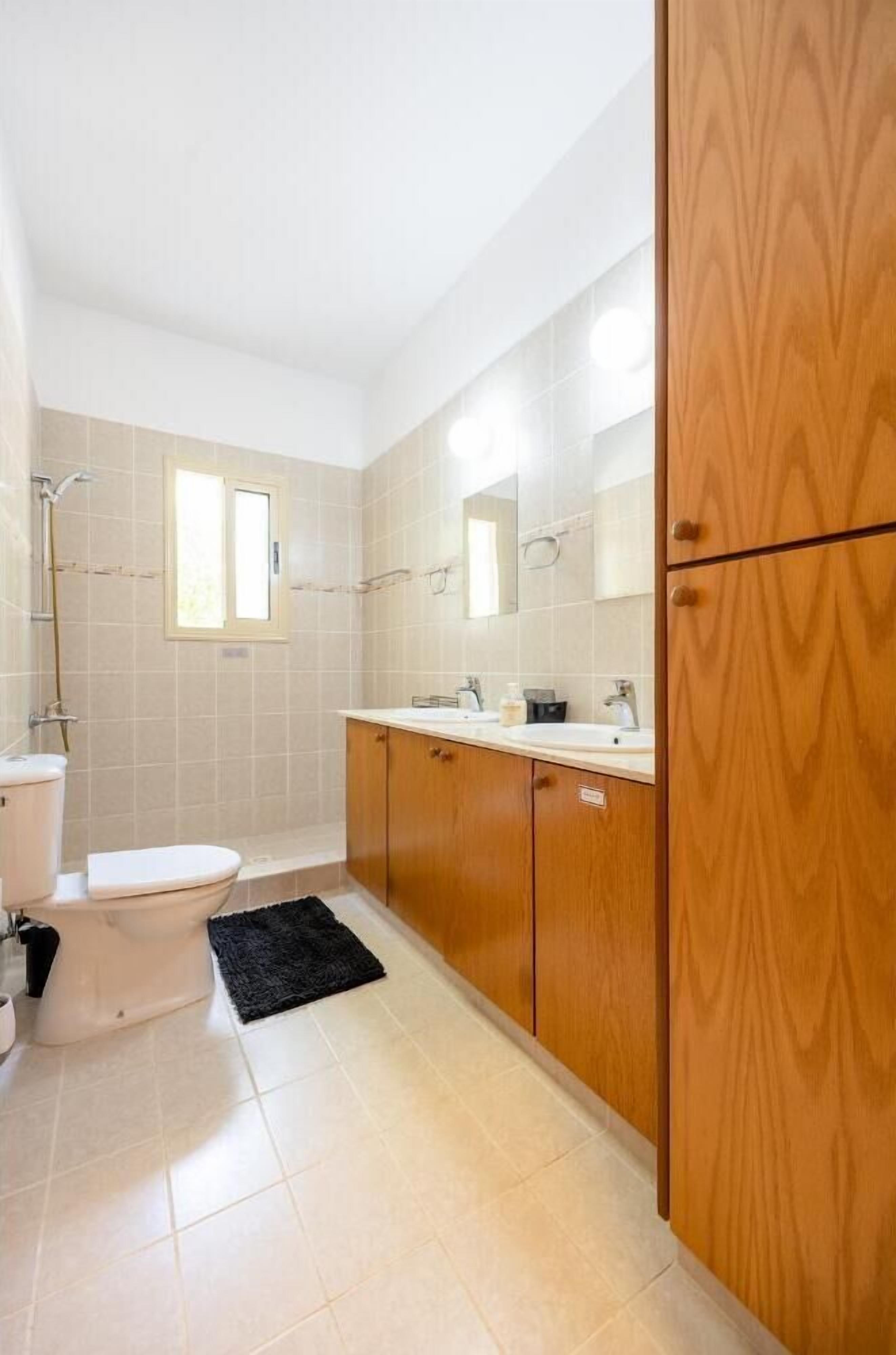 A bathroom with a toilet, sink, mirror, and wooden cabinets.