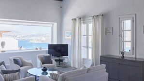 A modern living room with a large window, a flat-screen TV, and a seating area with a glass coffee table. - Aegean Scent  (Mykonos)