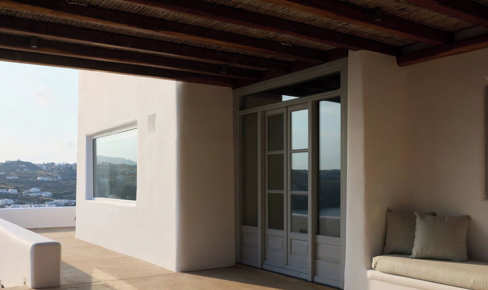 A balcony with a view of a hillside, a sliding glass door, and a beige sofa.