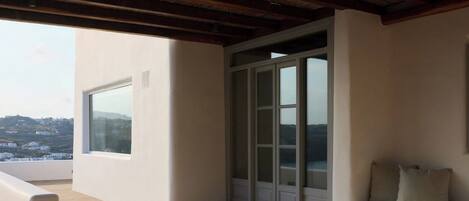 A balcony with a view of a hillside, a sliding glass door, and a beige sofa.