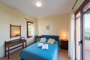 A bedroom with a large bed, a bedside table, a dresser, a mirror, and a window with curtains. - Odysseus Villa in Plaka (Apokoronas)