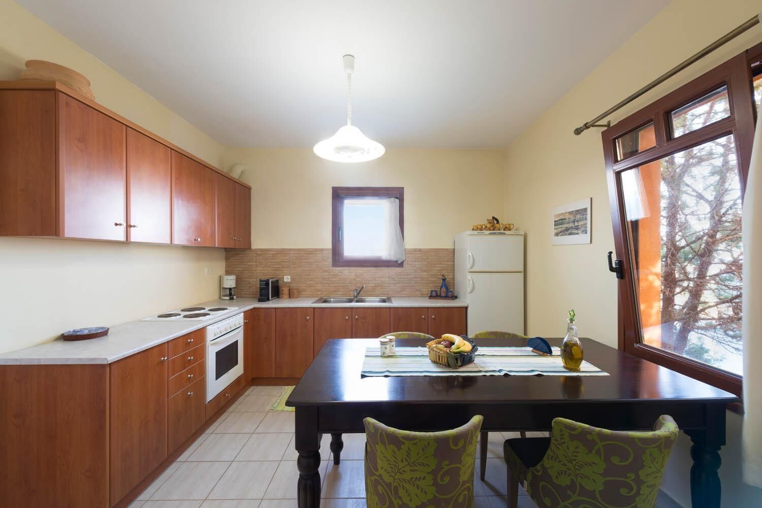 A compact kitchen with wooden cabinets, a central island, a refrigerator, and a dining area with chairs.