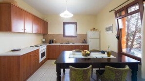 A compact kitchen with wooden cabinets, a central island, a refrigerator, and a dining area with chairs. - Odysseus Villa in Plaka (Apokoronas)