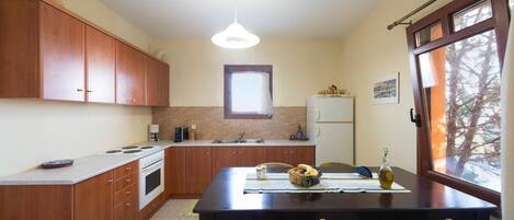 A compact kitchen with wooden cabinets, a central island, a refrigerator, and a dining area with chairs.