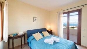 A bedroom with a bed, a nightstand, a framed picture, and a view of the sea through a sliding door. - Odysseus Villa in Plaka (Apokoronas)