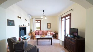 A living room with a sofa, a coffee table, a TV, and a fireplace. - Odysseus Villa in Plaka (Apokoronas)