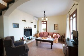 A living room with a fireplace, a sofa, a coffee table, and a TV. - Odysseus Villa in Plaka (Apokoronas)