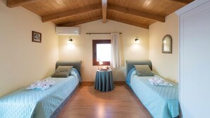 A bedroom with two single beds, a small table, and a window with curtains. - Villa Aphrodite in Plaka (Apokoronas)