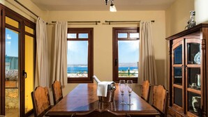 A dining room with a large table, chairs, and a view of the sea through two windows. - Villa Aphrodite in Plaka (Apokoronas)