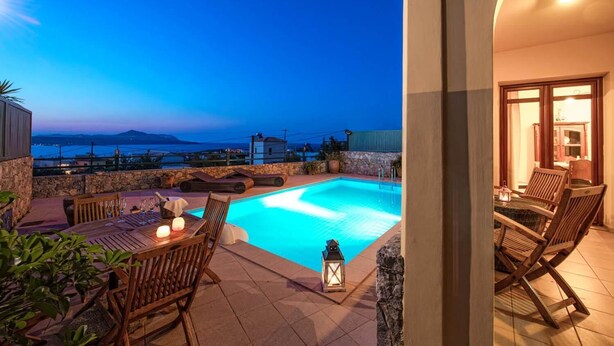 A pool area with a view of the sea, outdoor seating, and a stone wall. - Villa Aphrodite in Plaka (Apokoronas)